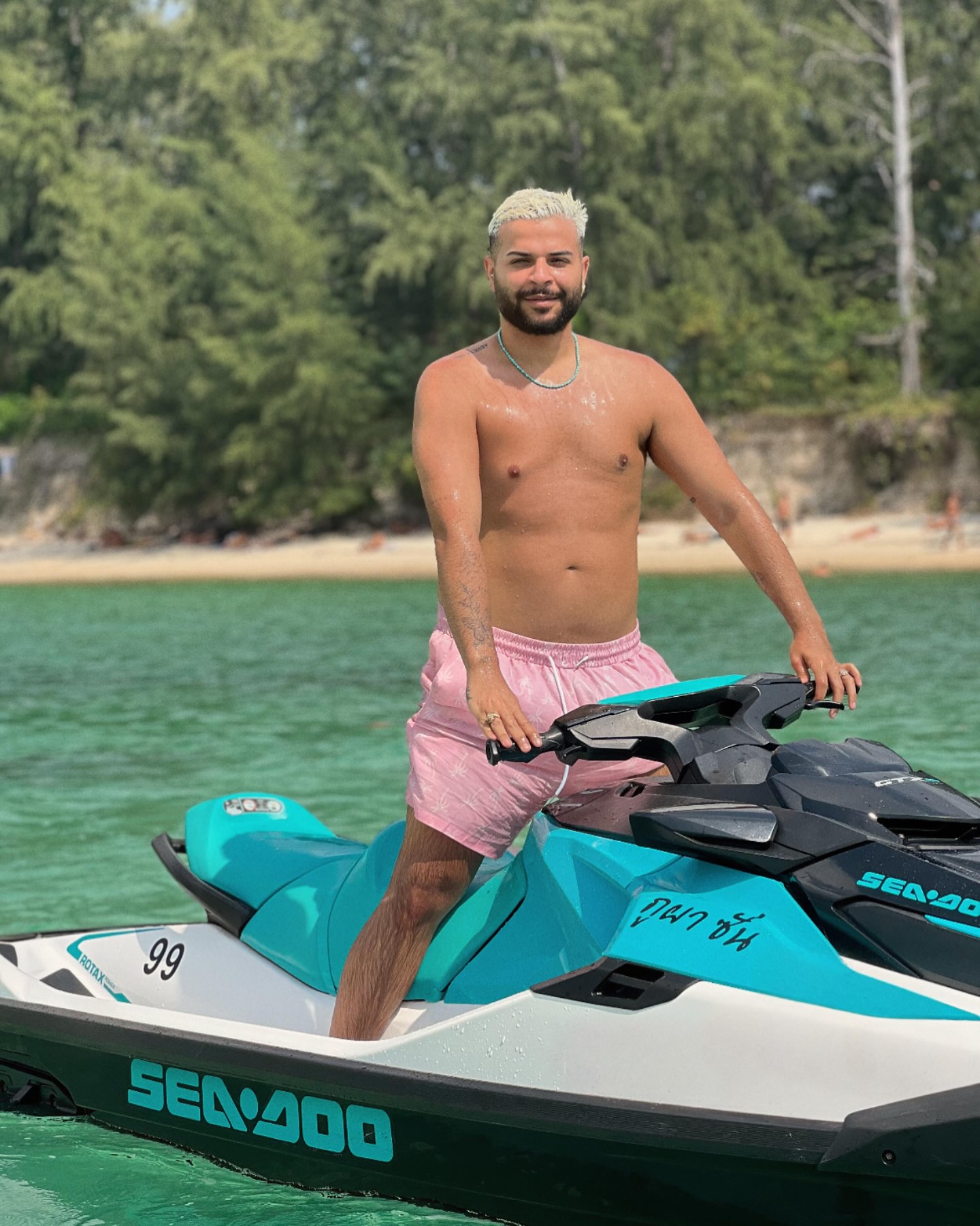 Rider standing on a turquoise Sea-Doo jet ski in shallow green water in Koh Samui