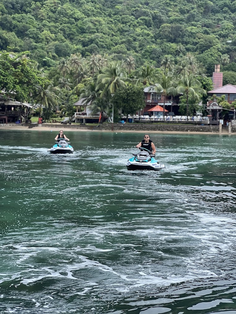 Two Sea-Doo jet skis cruising back toward a palm-lined Koh Samui beach