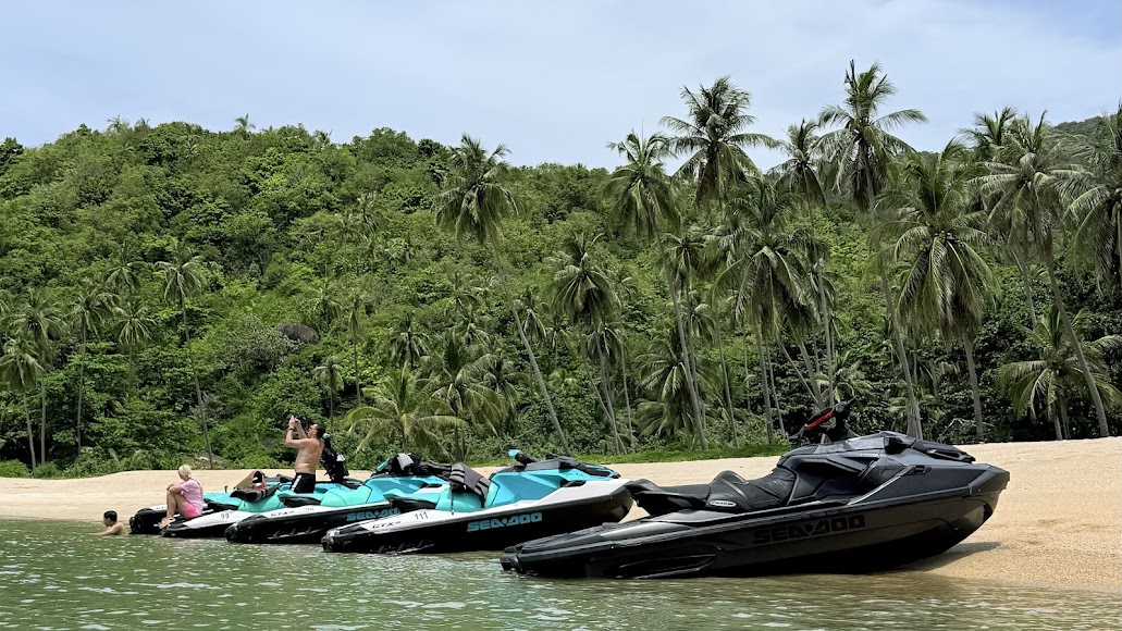Line of Sea-Doo jet skis pulled up on a palm-backed beach in the Koh Samui archipelago